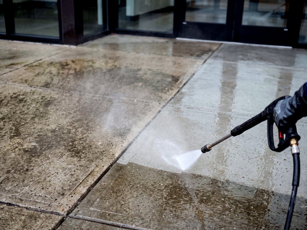 Pressure washing a commercial concrete entry walkway, showing the line between grimy and cleaned concrete